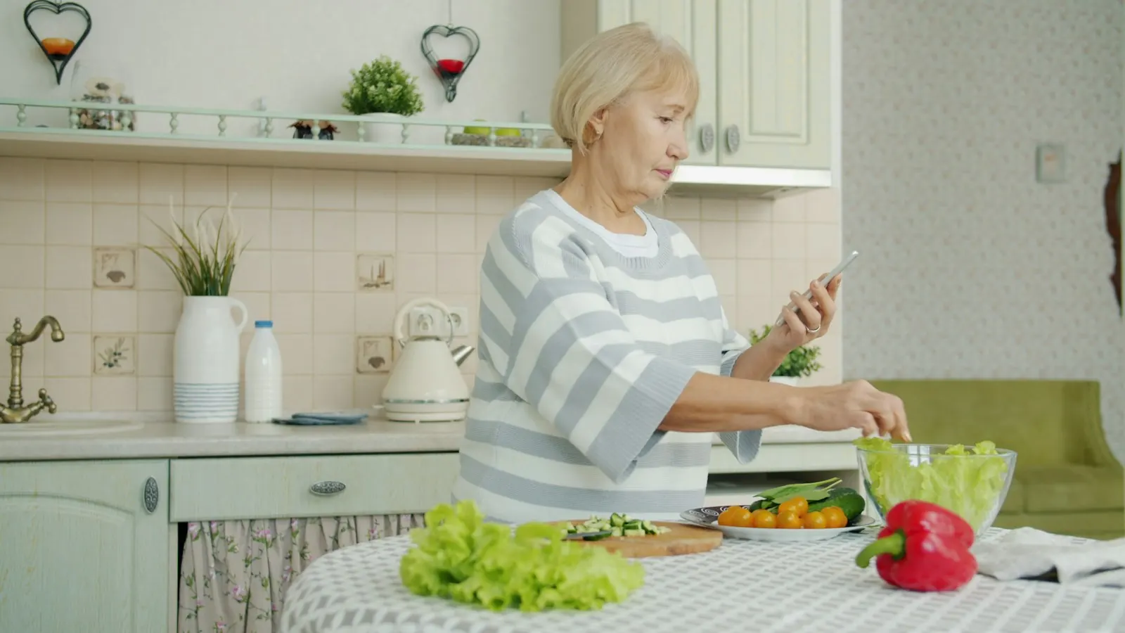 An older woman reading her phone at the kitchen counter