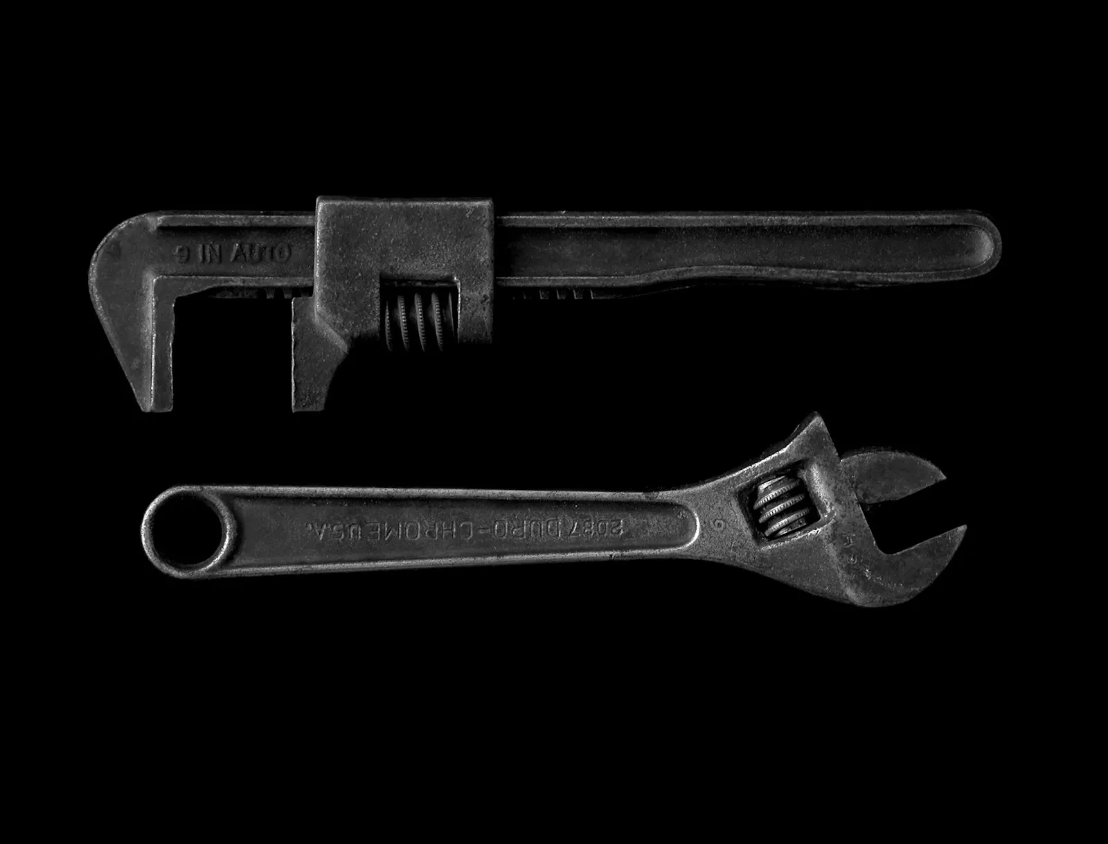 A pipe wrench and an adjustable wrench on a dark background