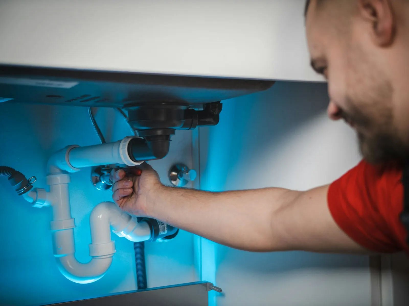 A plumber working on the pipes under a sink