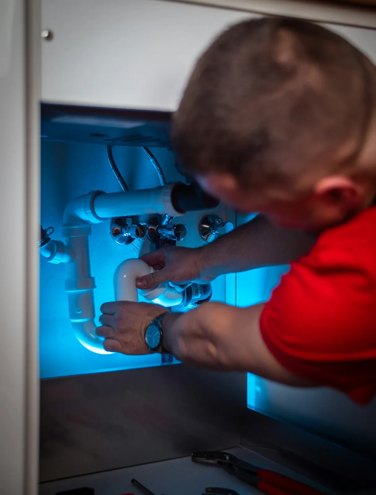 A plumber working on the pipes under a sink