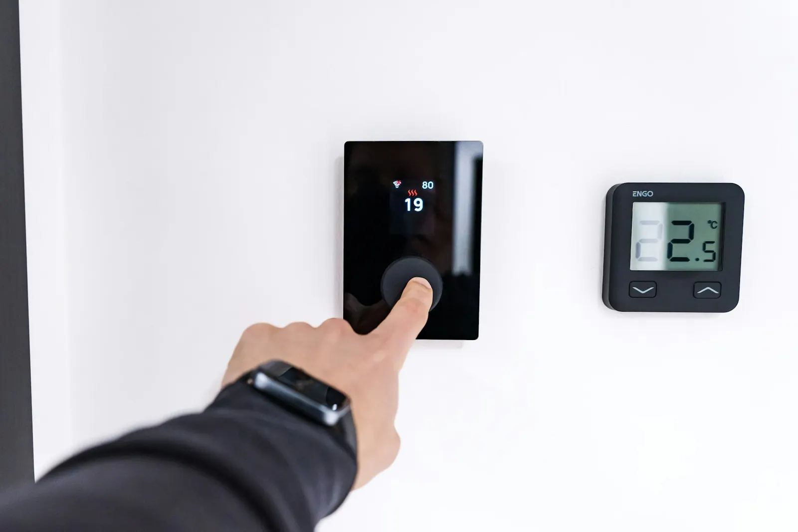 A hand adjusting a digital thermostat on a wall